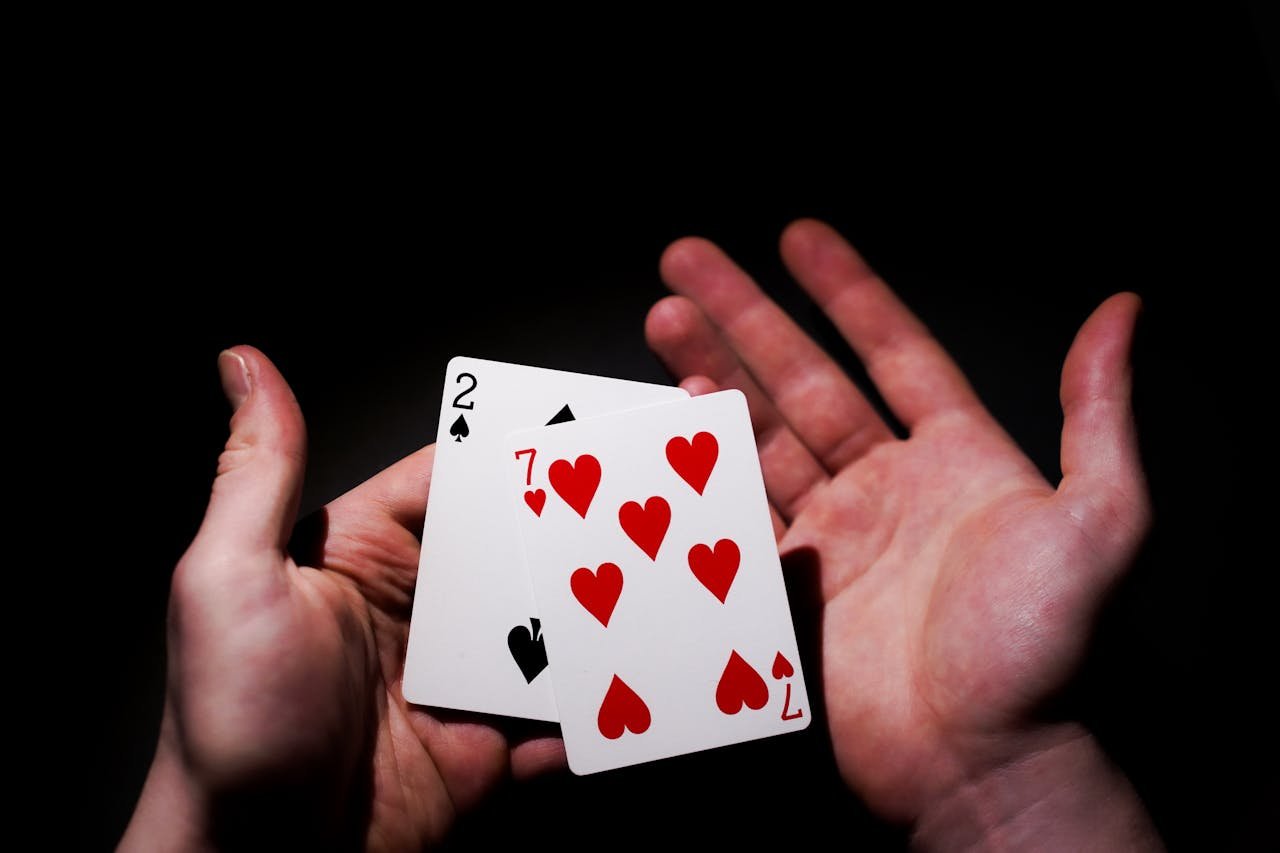 A pair of hands holding playing cards against a dark background.